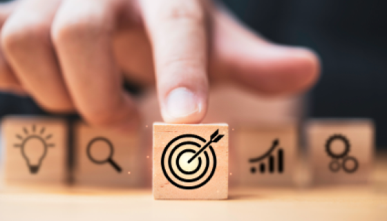 Finger pointing to a building block with a target on it.