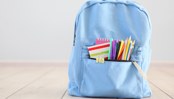 An image showing a blue children's backpack with coloured pencils and a notebook in the front pocket. 