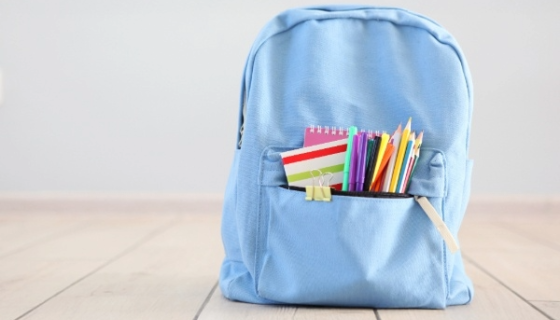 An image of a light blue kids backpack with coloured pencils and notepads in the front pocket.