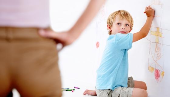 Preschool boy drawing on wall being discovered by an educator