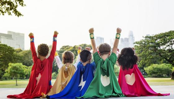 Children dressed as superheroes, two of them with arms held up