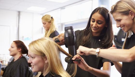 Female student assists with drying a client's hair in a hair salon