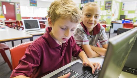 Primary school boy and girl in red school uniforms using computer at school
