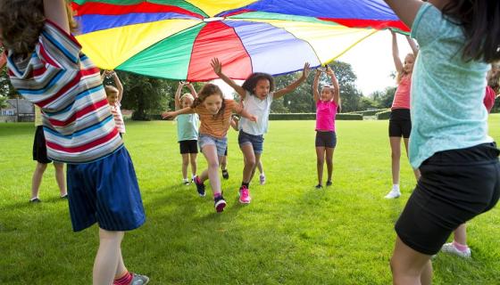Primary school children wearing short and t-shirts playing with a parachute on grasson a 