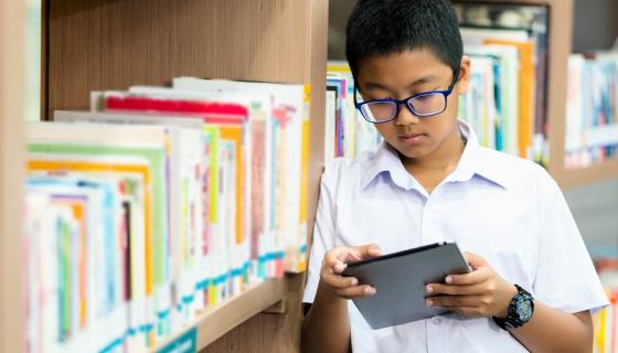 Young male international student in library looking at a tablet